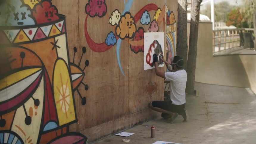 A man uses a stencil to spray paint on a building wall on a sunny day