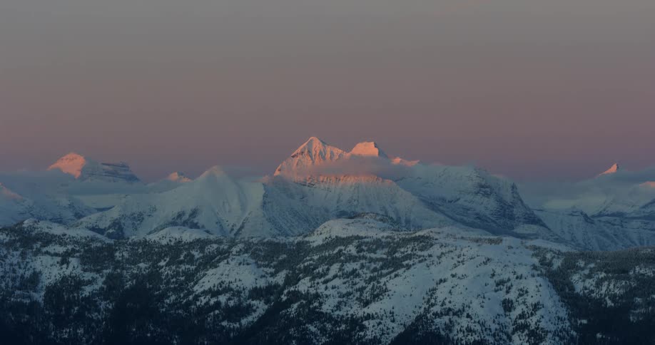 The sun shines on the peaks of snow covered mountains at sunset