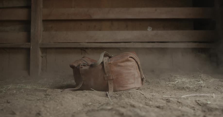 A leather satchel falling onto a dirt floor