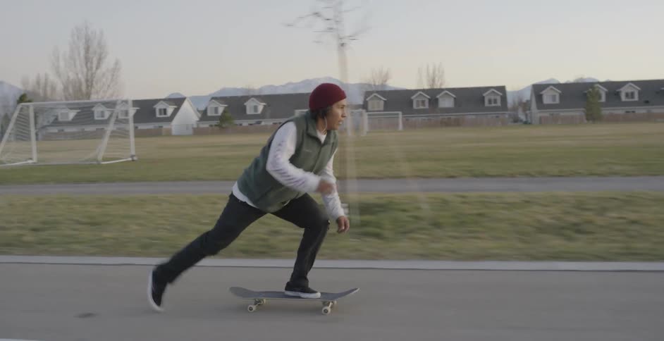 A boy is skateboarding down a road and then hops his board on to a bench