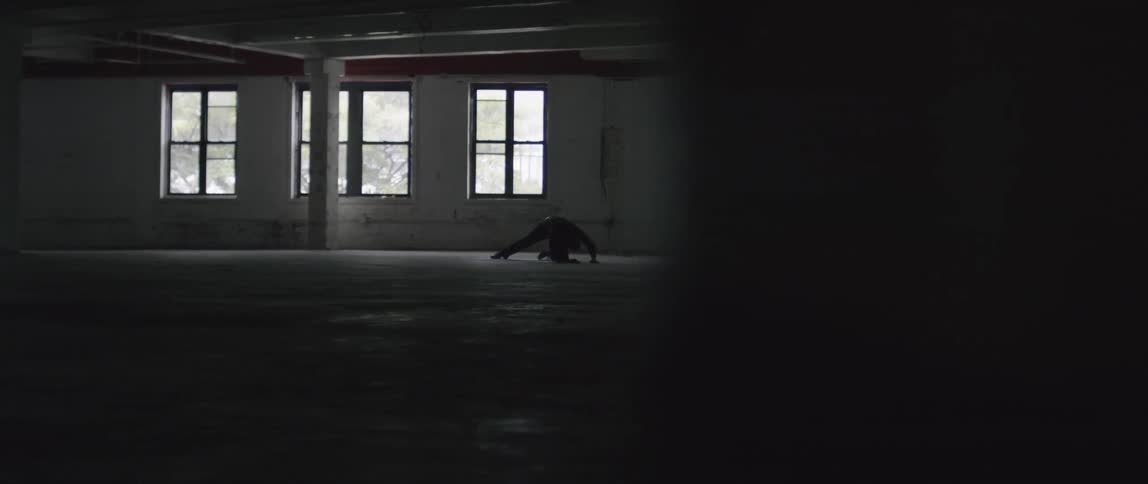 Two people inhabit an empty room one on the ground and one standing slightly bent over