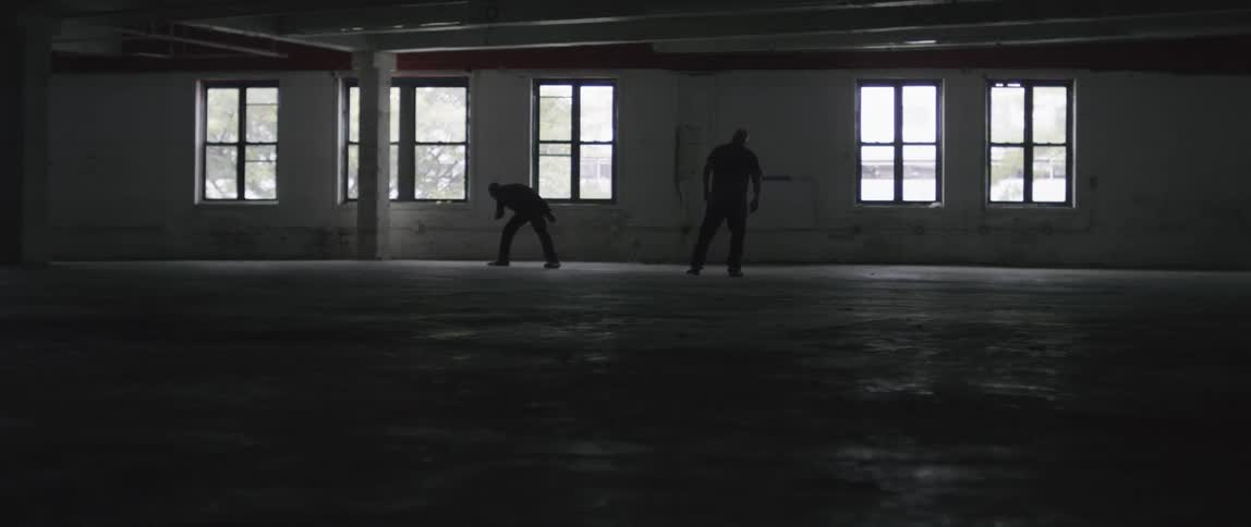 A man throws another off of him during a fight in an empty building