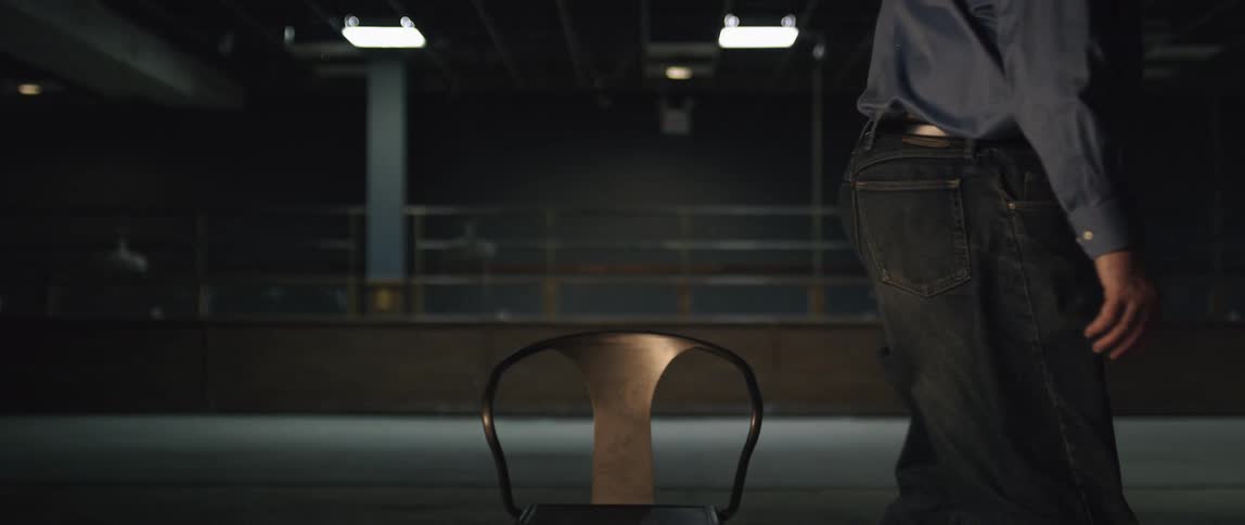 Man in a large dimly lit room gets up and walks from a metal chair