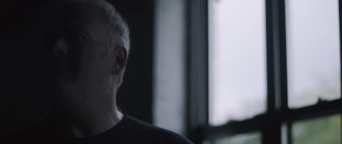 A man sits in a dark room by the window