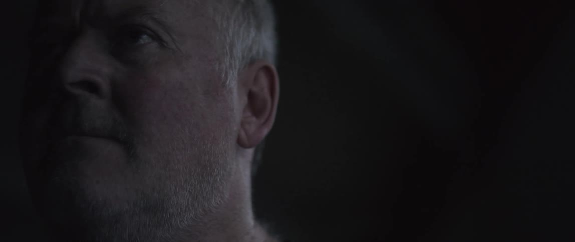 A man lifts his head in a dark room