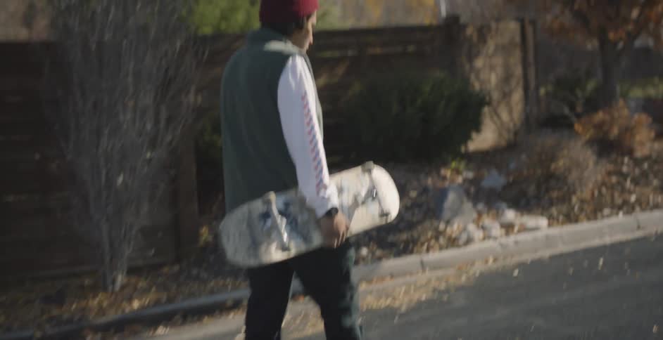 A man is walking in the road carrying a skateboard