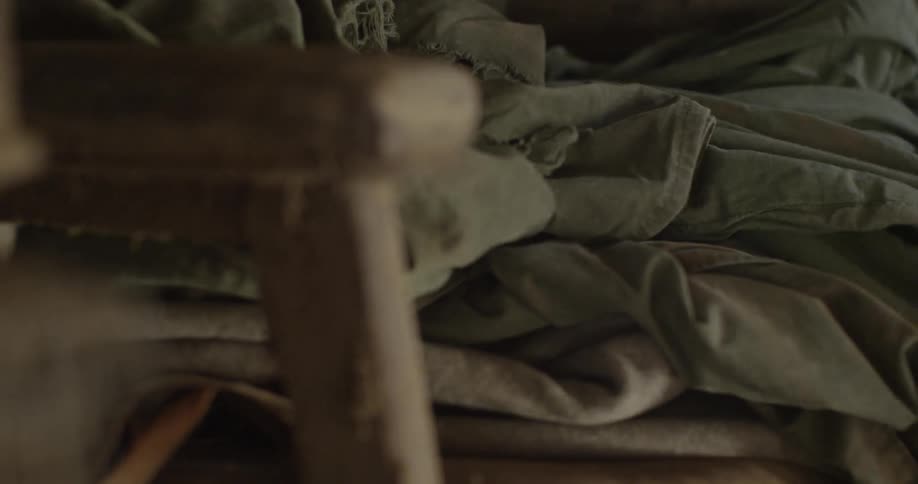 Old rags and fabric are being piled onto a wooden chair