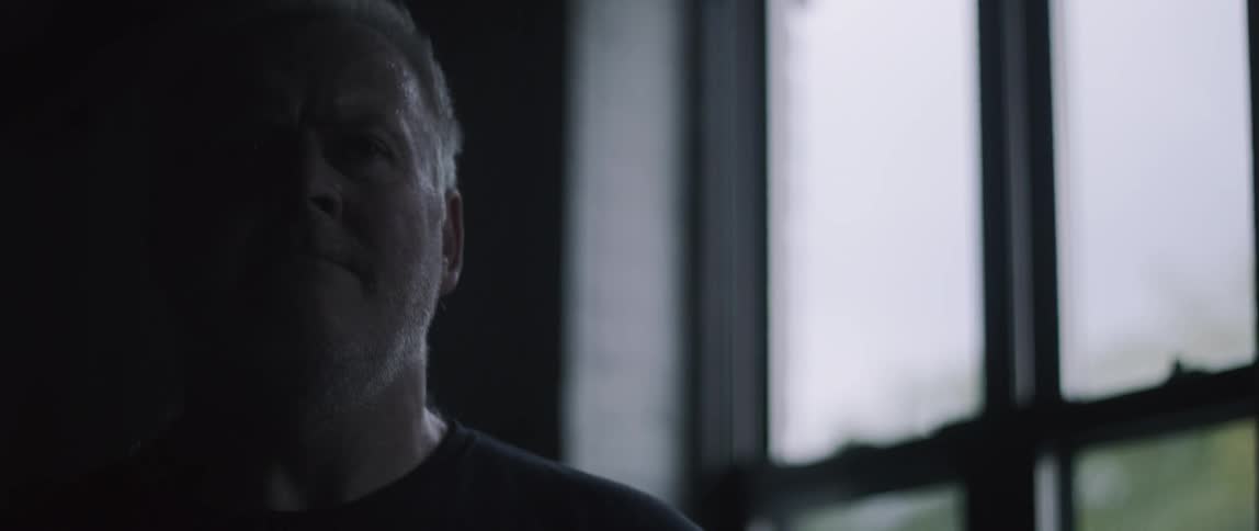 An old man turning his head while standing in a dark room