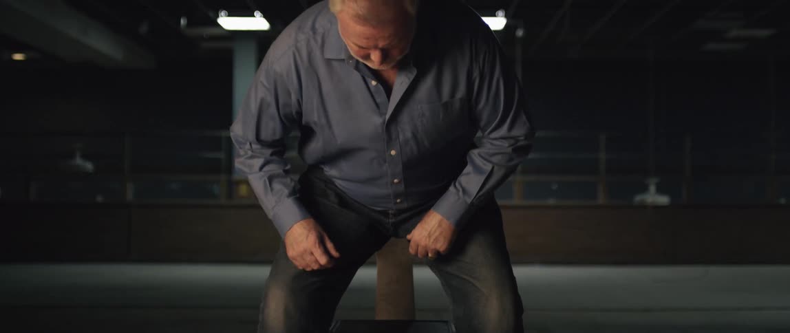 A man walking towards a chair and sitting down