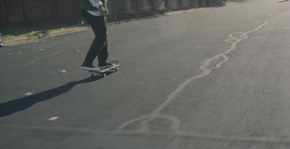 A man pushes off and skateboards down a neighborhood street on a sunny fall day