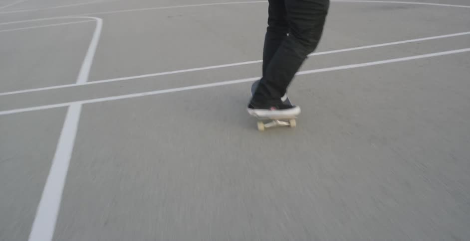 A male jumps on his skateboard and successfully lands a trick while skating across a basketball court at a park