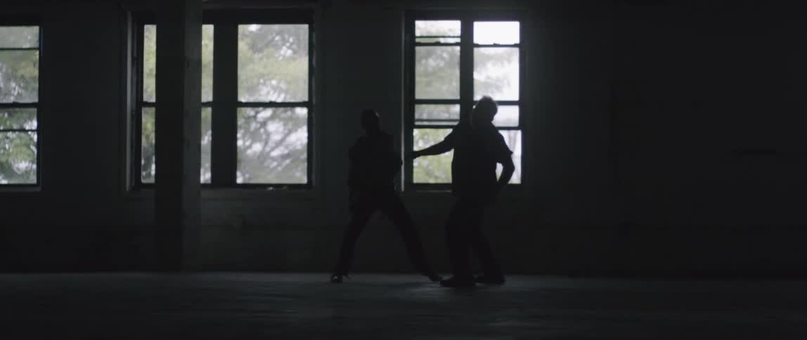 Two men fighting in an empty room with windows