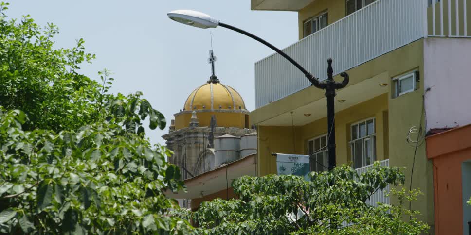 Beyond trees and buildings there is  a church (Parroquia Santiago Apostol)