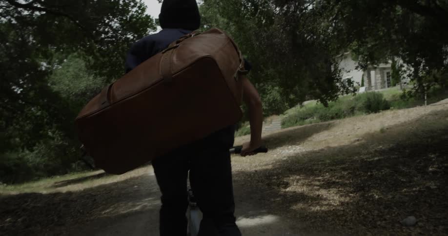 A person carrying a large bag rides a bike down a tree lined path