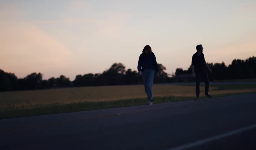 A man and woman walk down the road at sunset