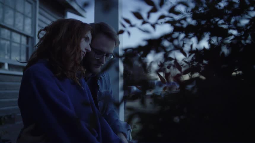 A man and a woman sit together on a porch supporting one another