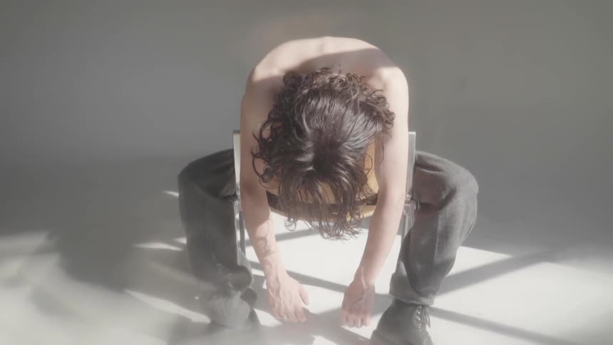 A person sits backwards in a chair slumped over with their hands almost touching the floor