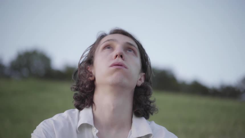 A man sits in a grass field with his eyes closed