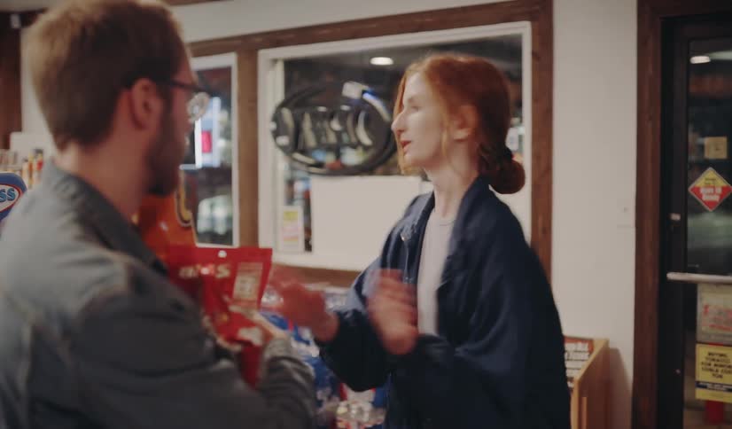 A woman hands a man some bags of chips and they run out the door