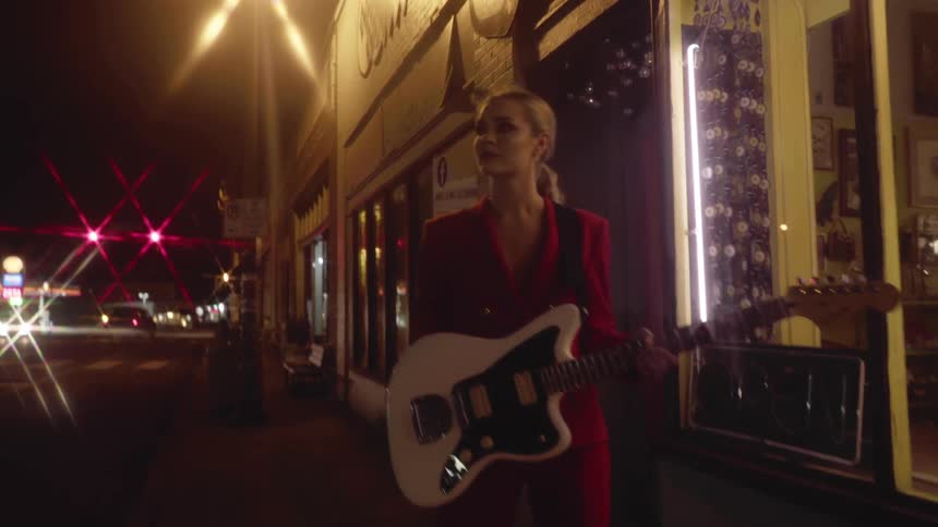 A woman is outside of a store holding a guitar