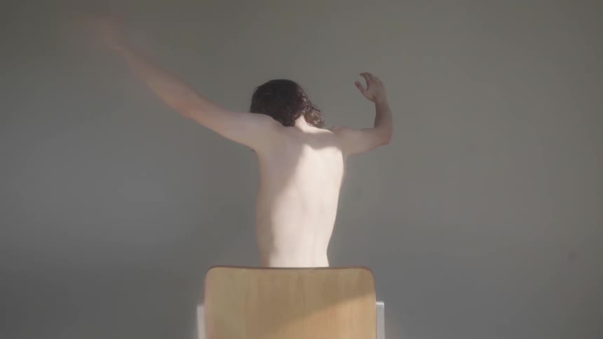 A shirtless man sitting in a chair and performing shoulder exercises