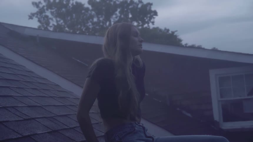 A woman sitting on a house roof at dawn