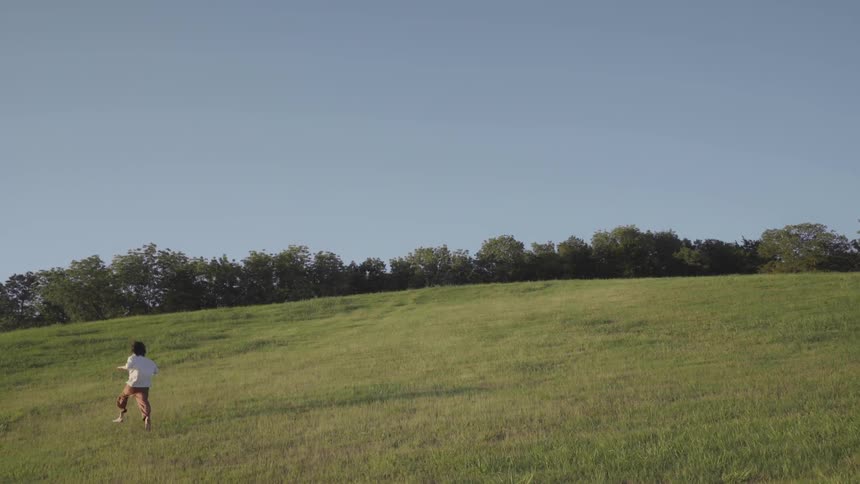 A child runs up a large hill near trees