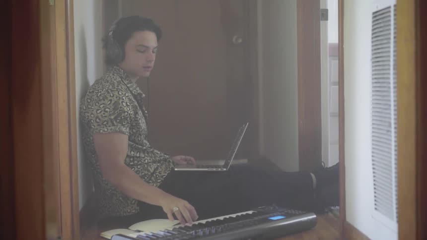 A man plays a keyboard while sitting on the floor in a hallway