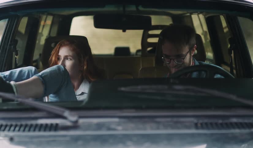 Man and woman talk while casually seated in the front of a car