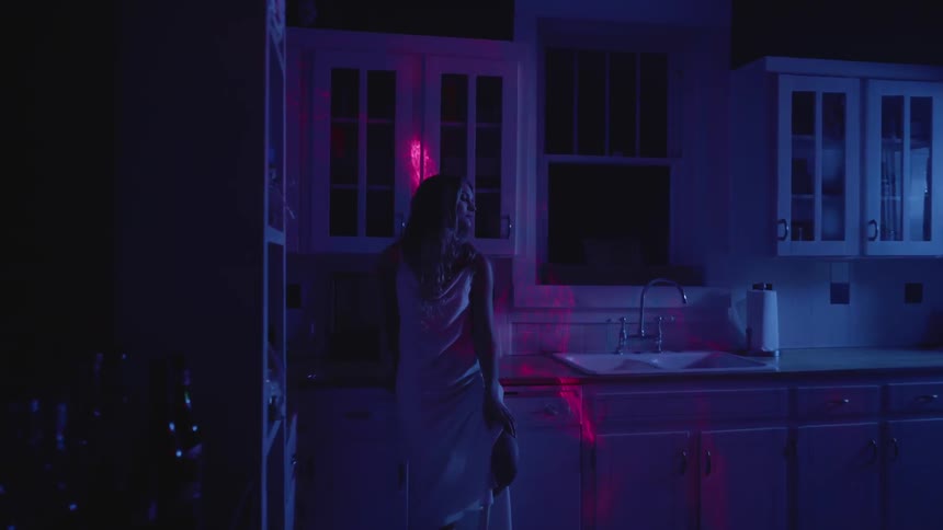 Red lights play over a woman in her kitchen at night
