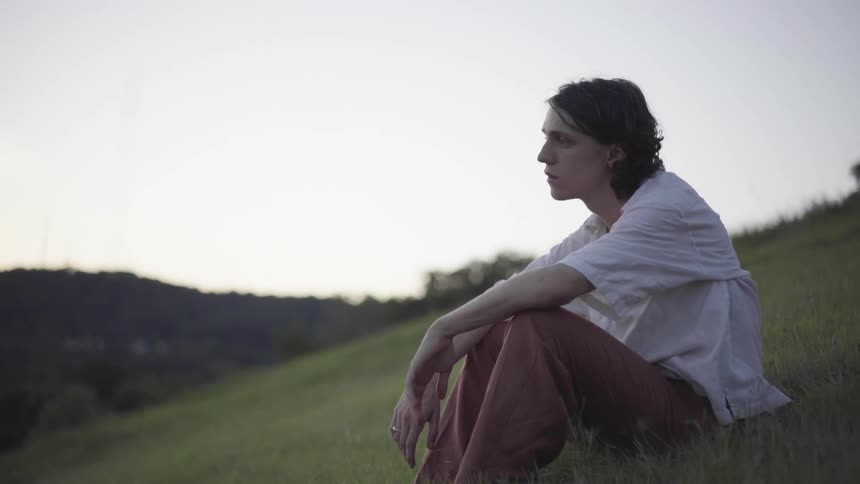 A man sits on a hill and looks into the distance