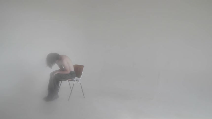Person sits on chair with head down in smoky empty room