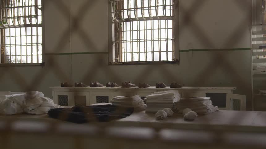 Linens and shoes lines up on tables behind a fence in a prison room