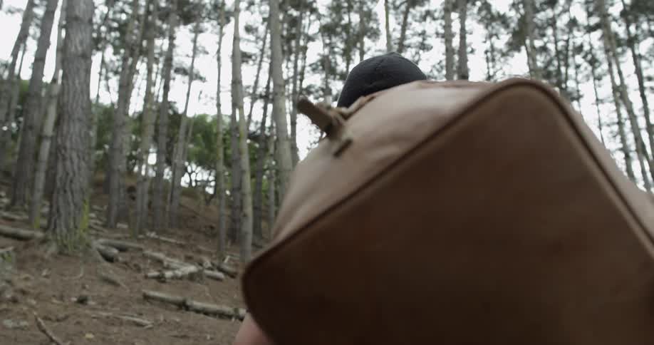A man hikes up steep tree filled hill carrying a bag