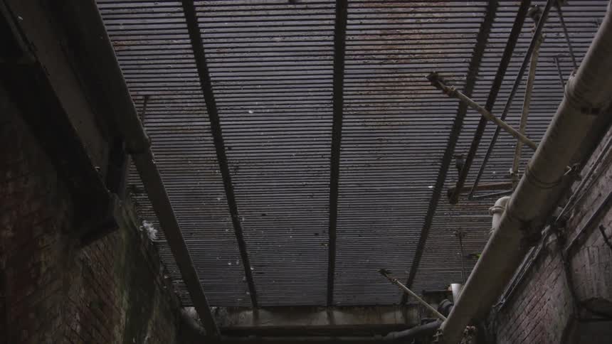Brackets and pipe are attached to a metal grate above an alley