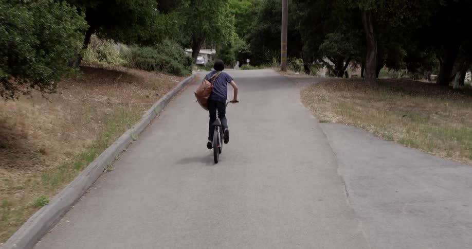 A boy riding a bicycle up a mildly inclined street
