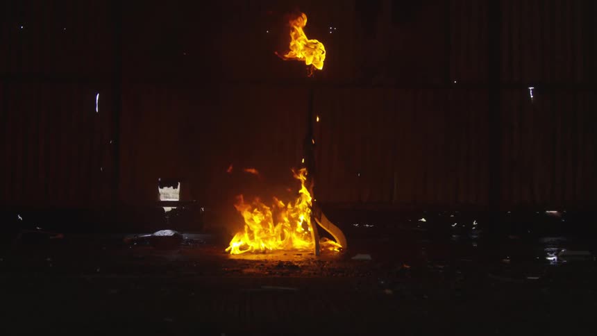 Fire burns a tall object in a dim room