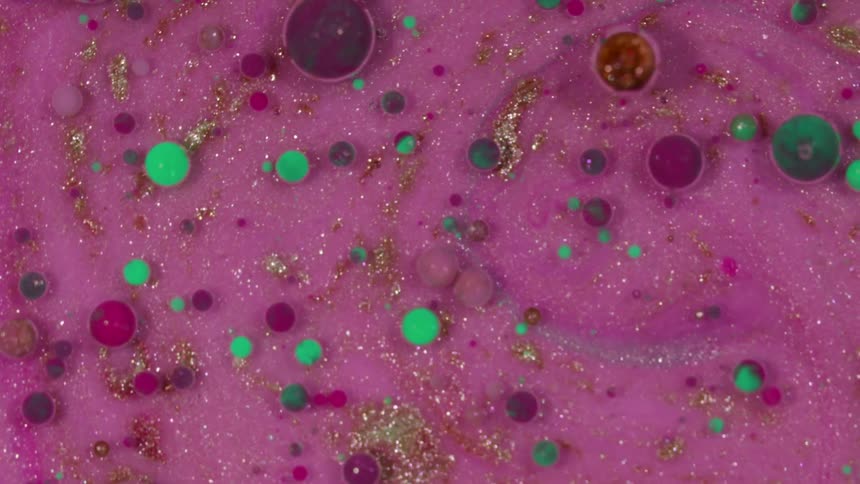 Marbles float on top of a thick pink and purple liquid filled with sparkles