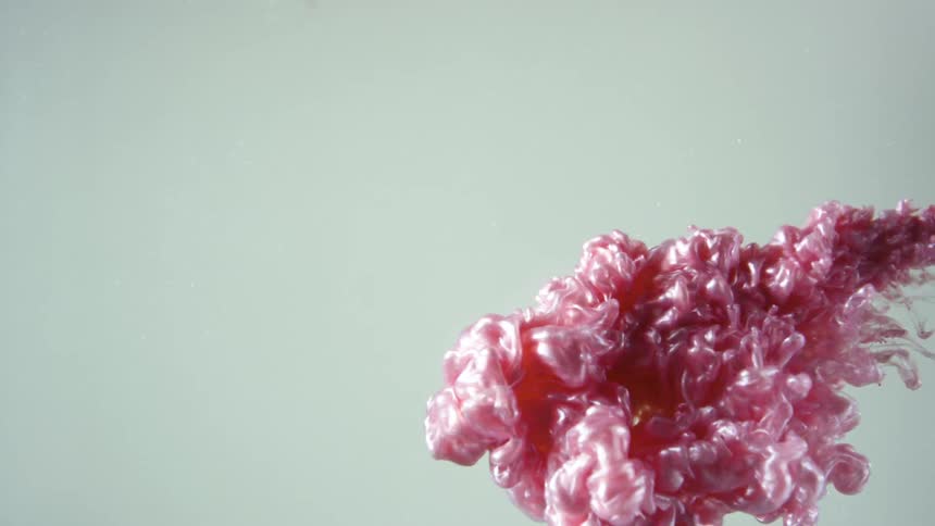 A pink liquid spreading through clear water from one side of the screen to the other