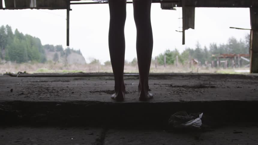 Girl in short dress and barefoot standing in vacant barn
