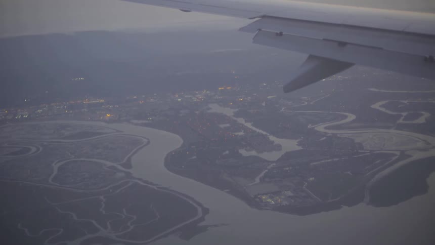 An airplane wing is visible as a plane flies over lakes and towns during a cloudy dusk