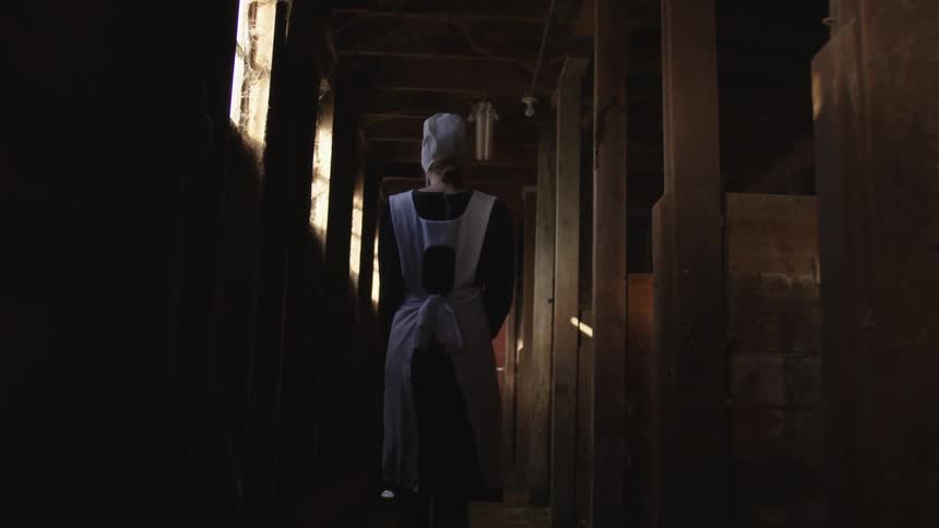 A woman wearing the uniform of a nurse walks along the corridor of a wood beamed building with high windows