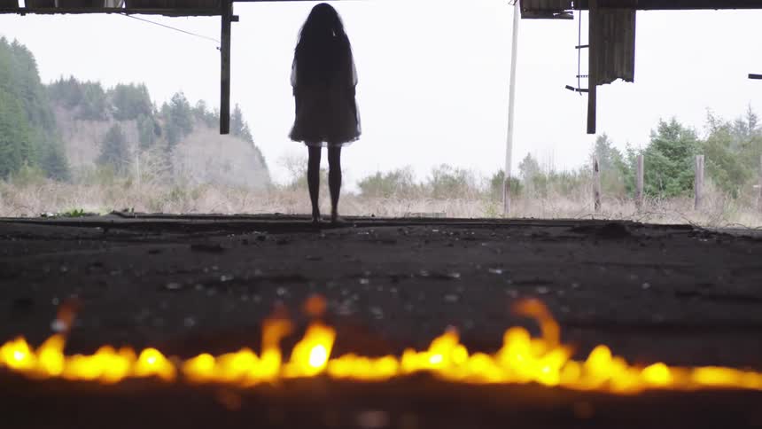 A girl stands near a fire burning on the ground