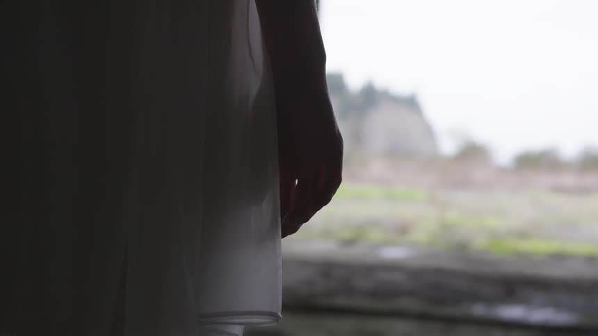 A girl in a white dress stands in an abandoned building