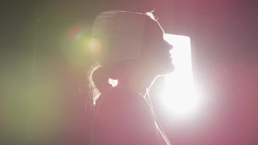 Woman stands in a dark room illuminated by a very bright light