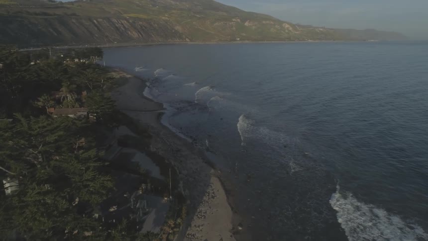 Ocean waves come to shore near homes and palm trees