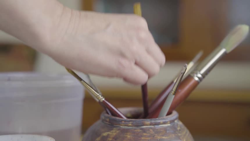 Hand picks up the paint brush from the jar