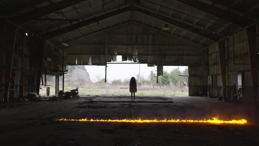 A girl stands near a fire burning on the ground