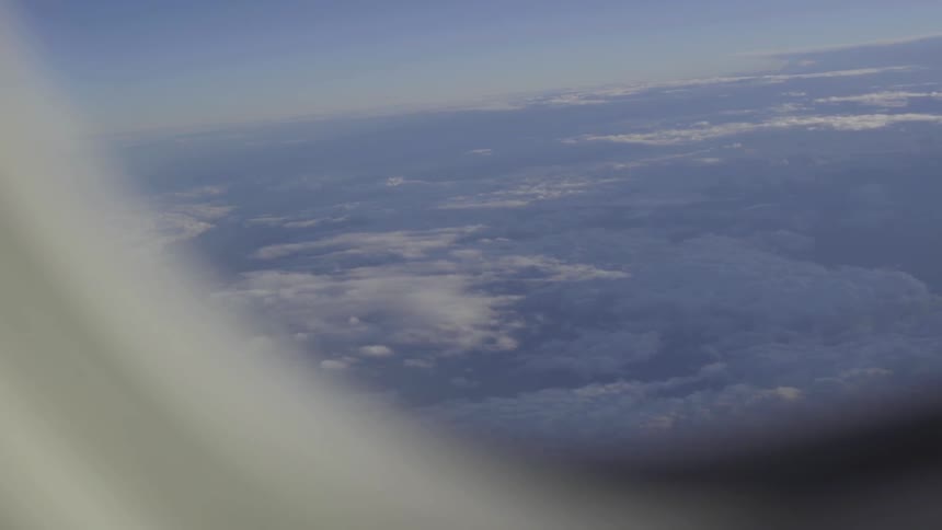 Outside of the plane window you can see the clouds above the fields