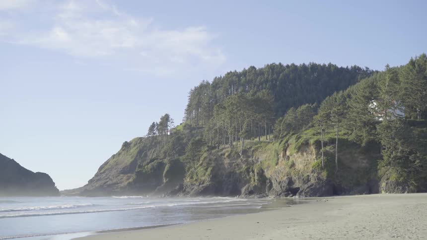 A view of a beach, the water and the cliff beside it